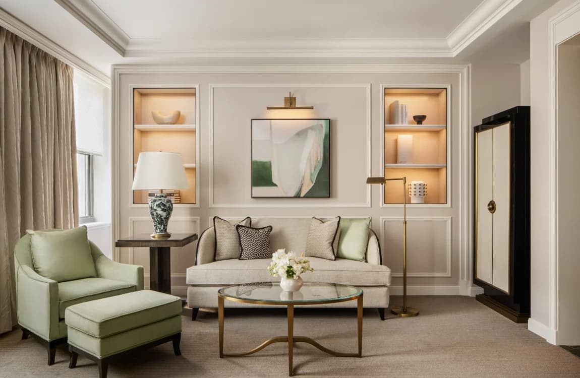 Elegant living room at Waldorf Astoria New York with cream sofa, green accent chair, illuminated wall niches, and brass coffee table