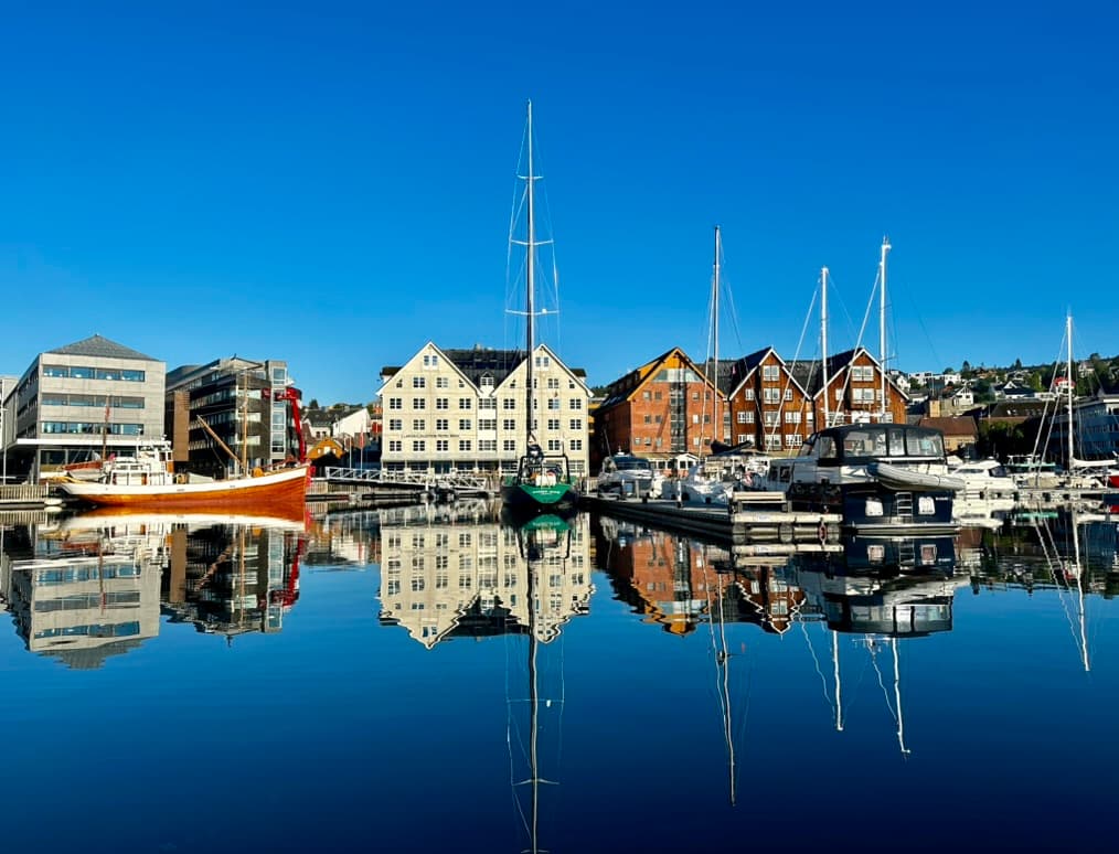 Colorful waterfront buildings reflected in still harbor water with moored sailboats in Norway