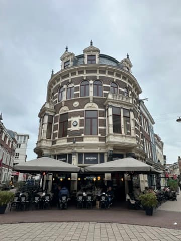 Ornate historic building with domed tower and outdoor café seating at street level in Amsterdam