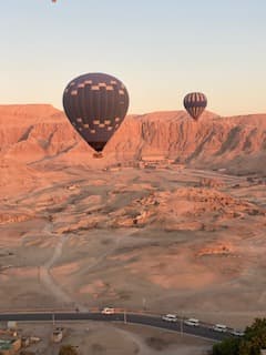 Two hot air balloons float above Egypt's desert landscape at sunrise, with a highway visible below