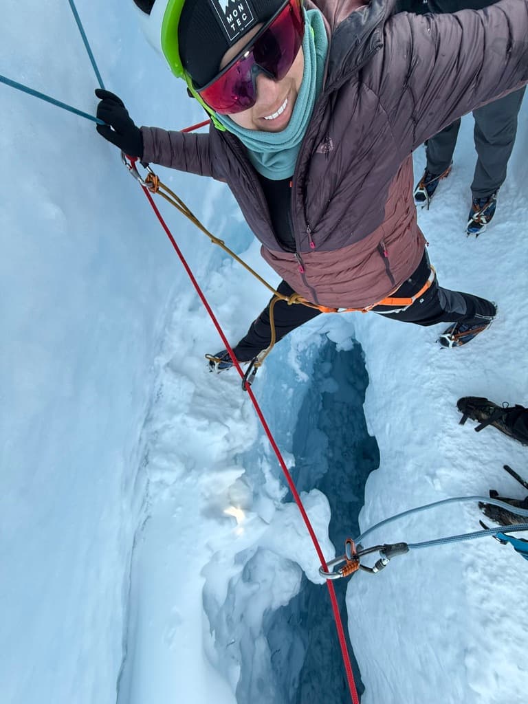 Diania Pimenta ice climbing in Antarctica, secured by red rope, smiling at camera above a crevasse