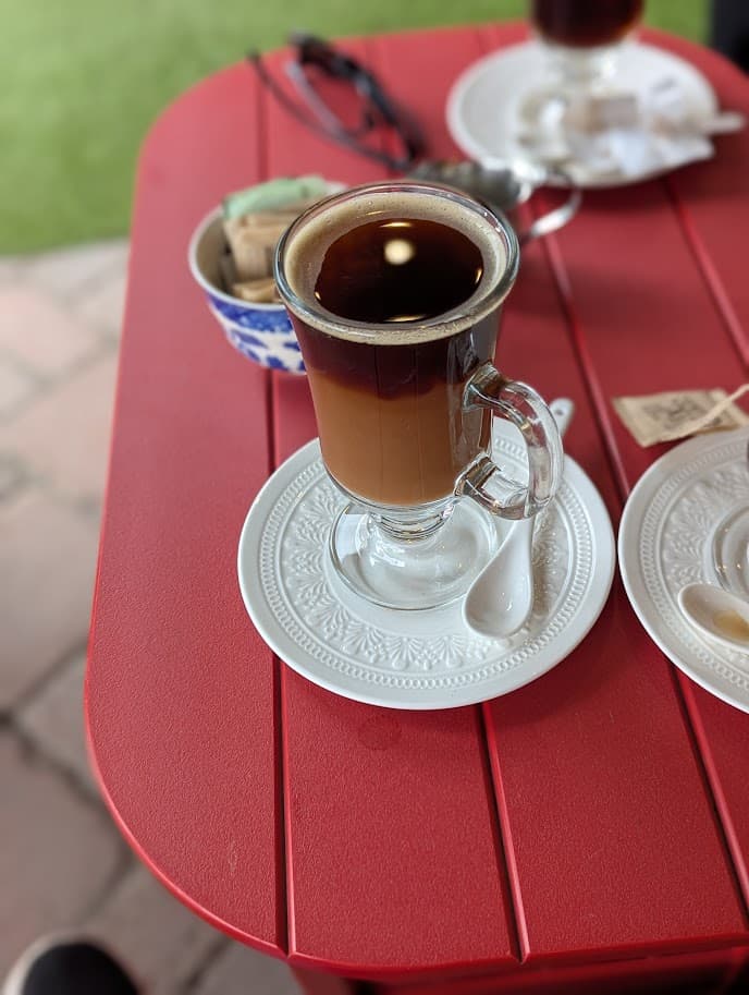 A glass of Irish coffee on a decorative white saucer at a red picnic table in Nova Scotia