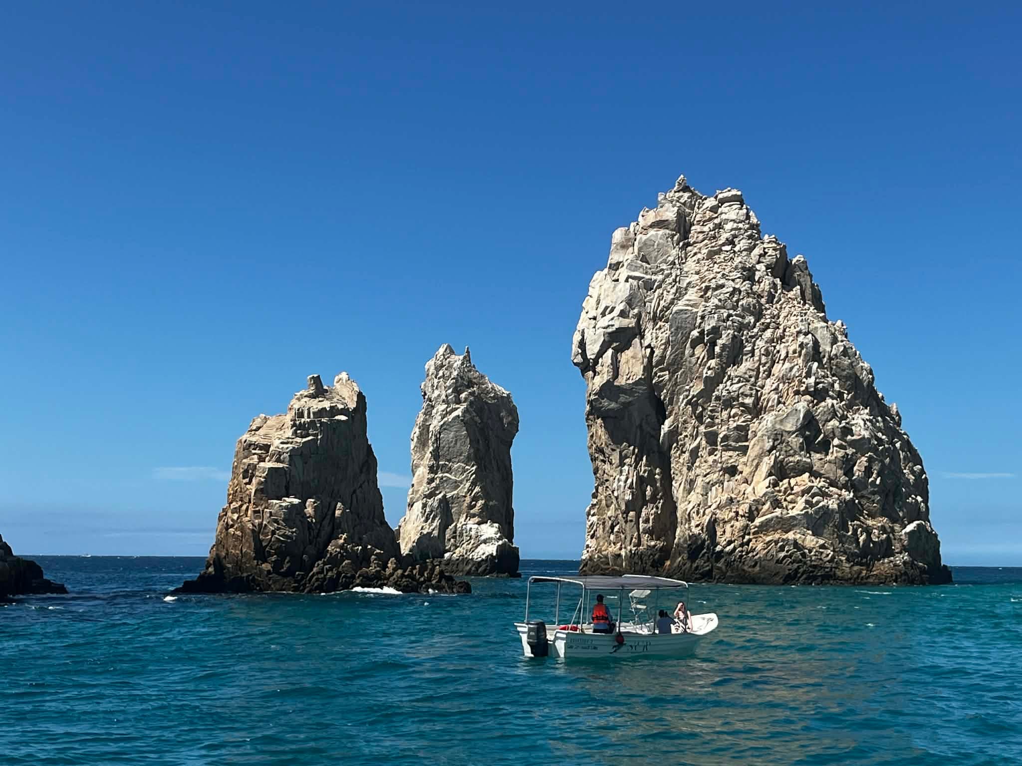 Dramatic rock formations rise from turquoise waters off Los Cabos with a small boat nearby