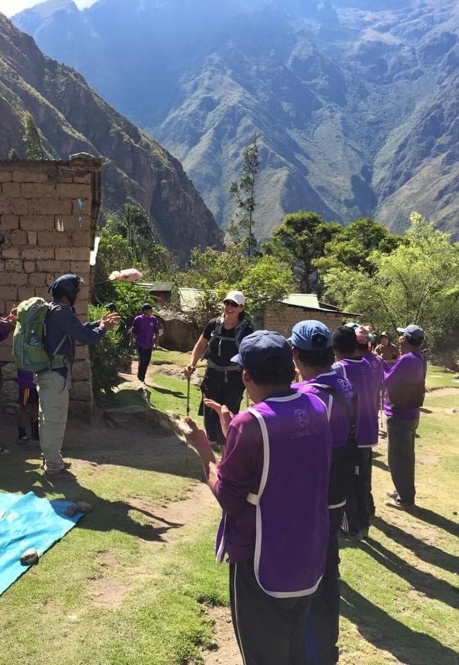 Tannis Dyrland stands with a group of hikers wearing purple shirts in a grassy valley surrounded by steep green mountains in Peru