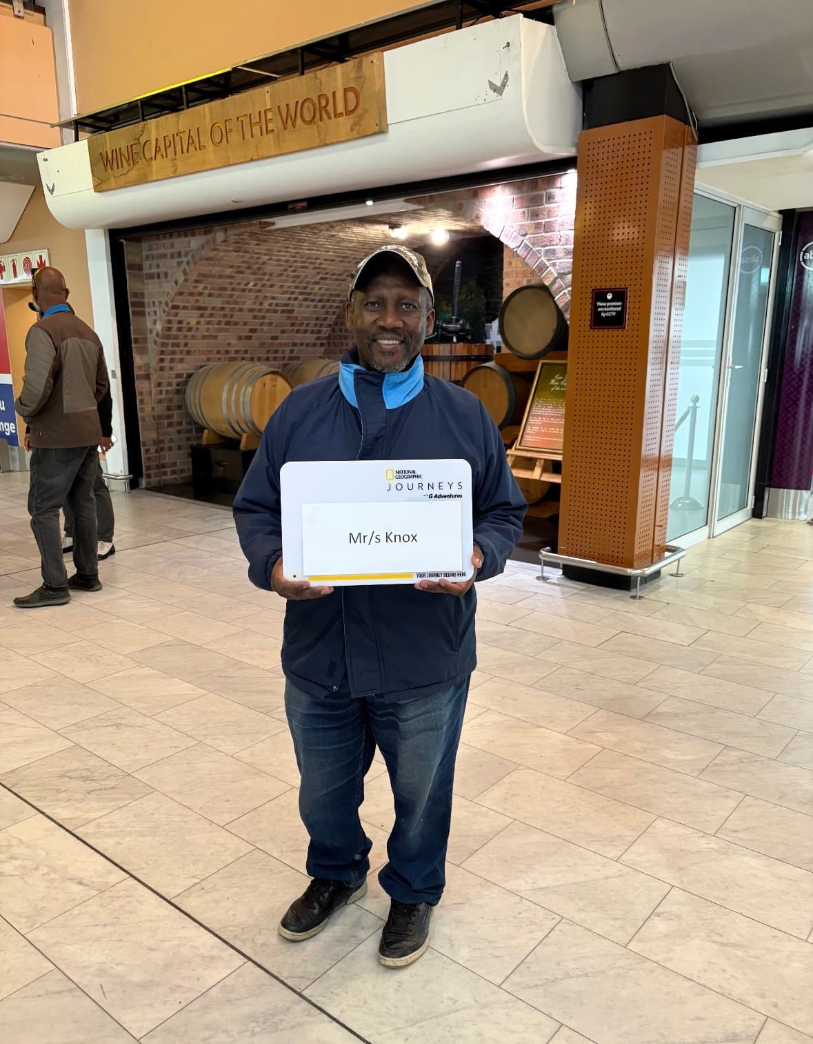 Man holding National Geographic Journeys certificate at wine capital display with wooden barrels in background