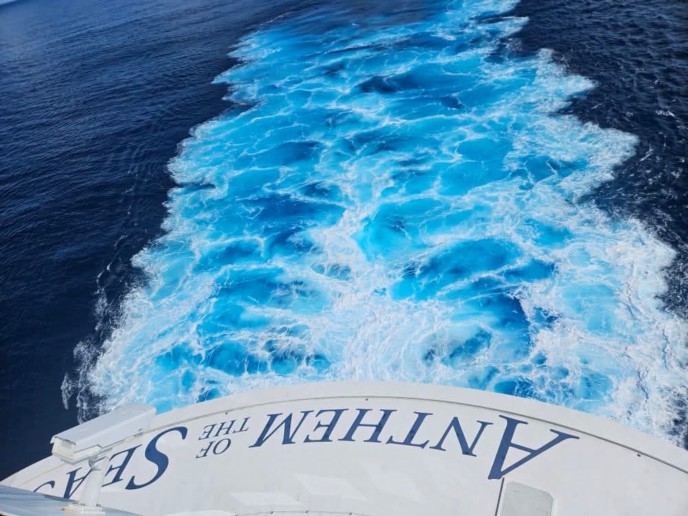 Wake churning behind Anthem of the Seas cruise ship in brilliant turquoise and white patterns on dark ocean