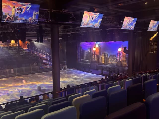 Theater seating area with multiple screens displaying colorful performance scenes on Symphony of the Seas